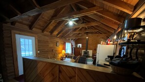 A wooden cabin interior with a kitchen area, dining space, and a large window. - Dreams End Woodcliff Cabin (Connersville)