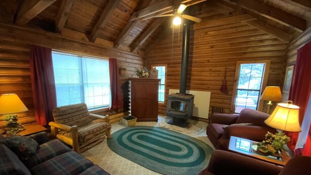 A cozy log cabin interior with a fireplace, plaid sofas, and a ceiling fan. - Dreams End Woodcliff Cabin (Connersville)