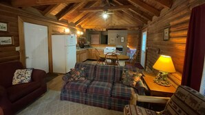 A cozy cabin interior with a sofa, a dining table, a lamp, and a kitchen area. - Dreams End Woodcliff Cabin (Connersville)