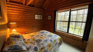 A wooden cabin room with a bed, a window, and a lamp. - Dreams End Woodcliff Cabin (Connersville)