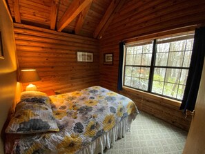 A wooden cabin room with a bed, a window, and a lamp.