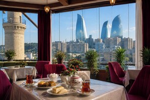 A dining area with a table set for two, a view of a cityscape with tall buildings, and a historic tower in the background. - Old Town Hotel (Baku)