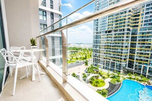 Ein Balkon mit weißen Stühlen und einem kleinen Tisch, mit Blick auf einen Swimmingpool und ein Wohngebiet mit hohen Gebäuden.