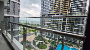 Un balcon avec une table et des chaises, une vue sur une piscine et, au loin, des immeubles de grande hauteur.