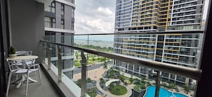 Un balcón con mesa y sillas, vistas a una piscina y edificios altos al fondo.