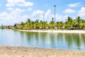 A beach resort with palm trees, a water body, and thatched-roof huts. - Lotus Bloom-Luxe Condo, Amazing View and Location! (Thành phố Hồ Chí Minh)