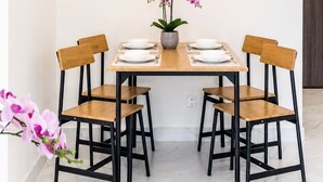Un coin repas avec une table dressée pour quatre personnes, entourée de chaises en bois à la structure noire. Au-dessus de la table, on peut admirer un grand tableau représentant des fleurs.