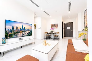 A modern living room with a large TV, a dining area, and a door leading to another room. - Lotus Bloom-Luxe Condo, Amazing View and Location! (Thành phố Hồ Chí Minh)
