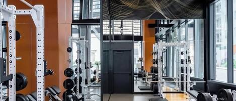 Un gimnasio con equipo de levantamiento de pesas, paredes con espejos y ventanas amplias.