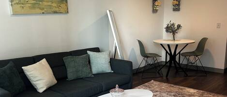 A modern living room with a dark sofa, a white coffee table, and a dining area with a round table and chairs.