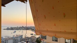 Un balcón con vistas a un puerto al atardecer, mostrando barcos y edificios.