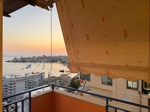Ein Balkon mit Blick auf einen Hafen bei Sonnenuntergang, mit Booten und Gebäuden.
