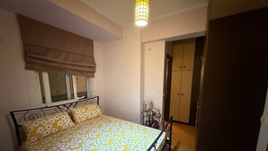 Un dormitorio con cama, ventana con persiana, mesita de noche con lámpara y armario.