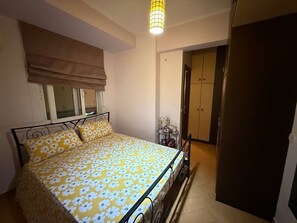 Ein Schlafzimmer mit Bett, Fenster mit Jalousie, Nachttisch mit Lampe und Kleiderschrank.