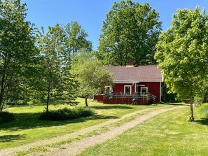 A red house with a tiled roof, surrounded by green trees and a grassy path leading to it. - 5 Person Holiday Home in Ruda (Ruda)