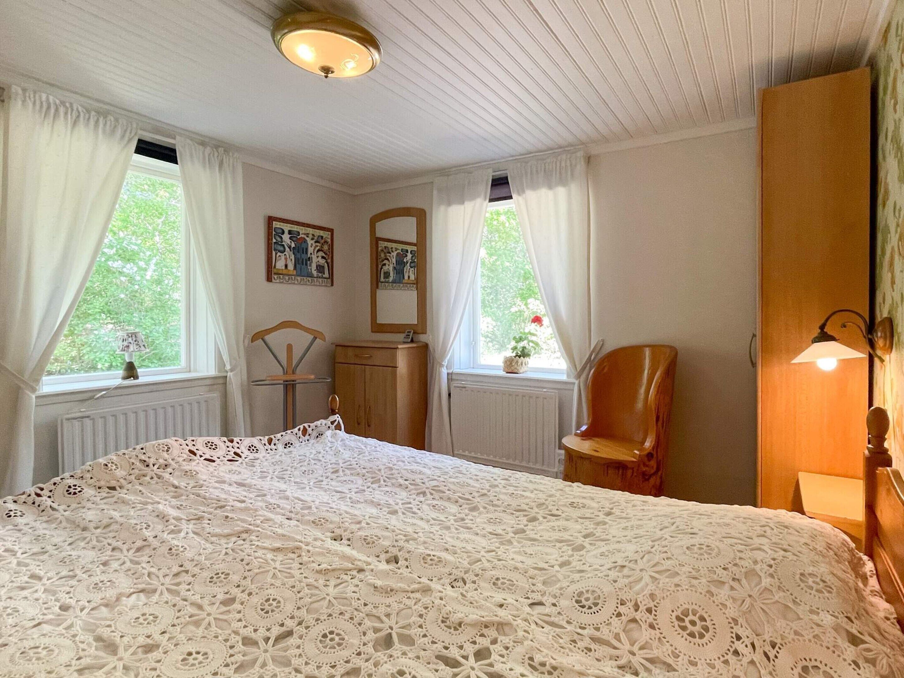 A bedroom with a large bed, a chair, a dresser, a mirror, and a window with curtains.