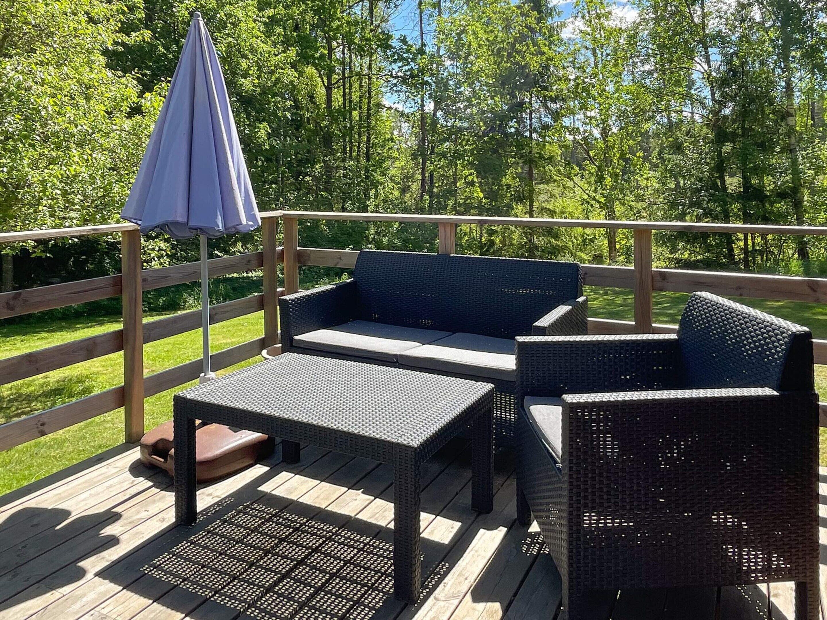 Um deck com móveis de vime, incluindo um sofá e uma mesa, e um guarda-sol azul.