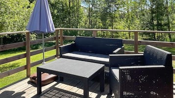 Um deck com móveis de vime, incluindo um sofá e uma mesa, e um guarda-sol azul.