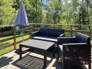 Eine Terrasse mit Korbmöbeln, darunter ein Sofa und ein Tisch, und einem blauen Sonnenschirm.