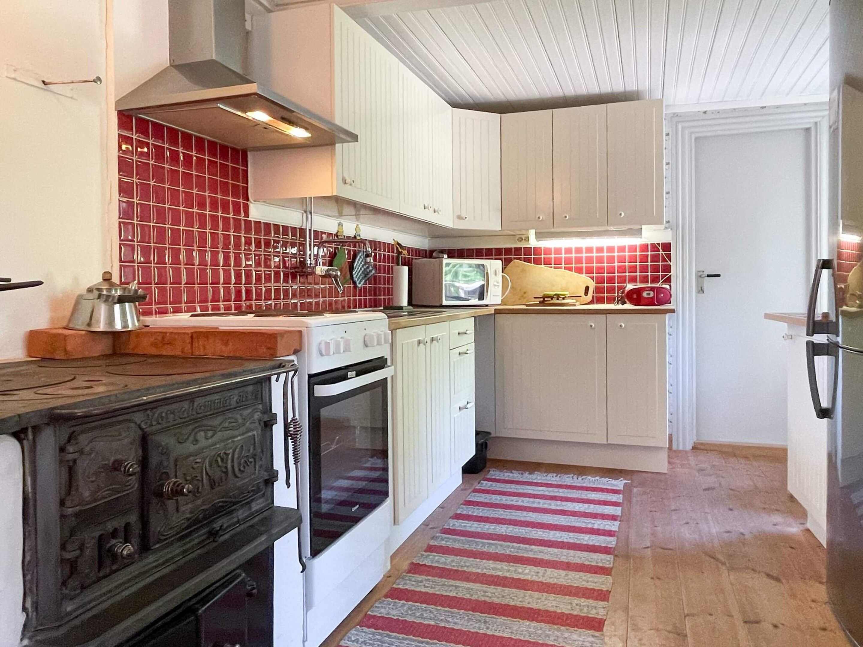 A kitchen with white cabinets, a red tiled backsplash, a stove, an oven, and a microwave.
