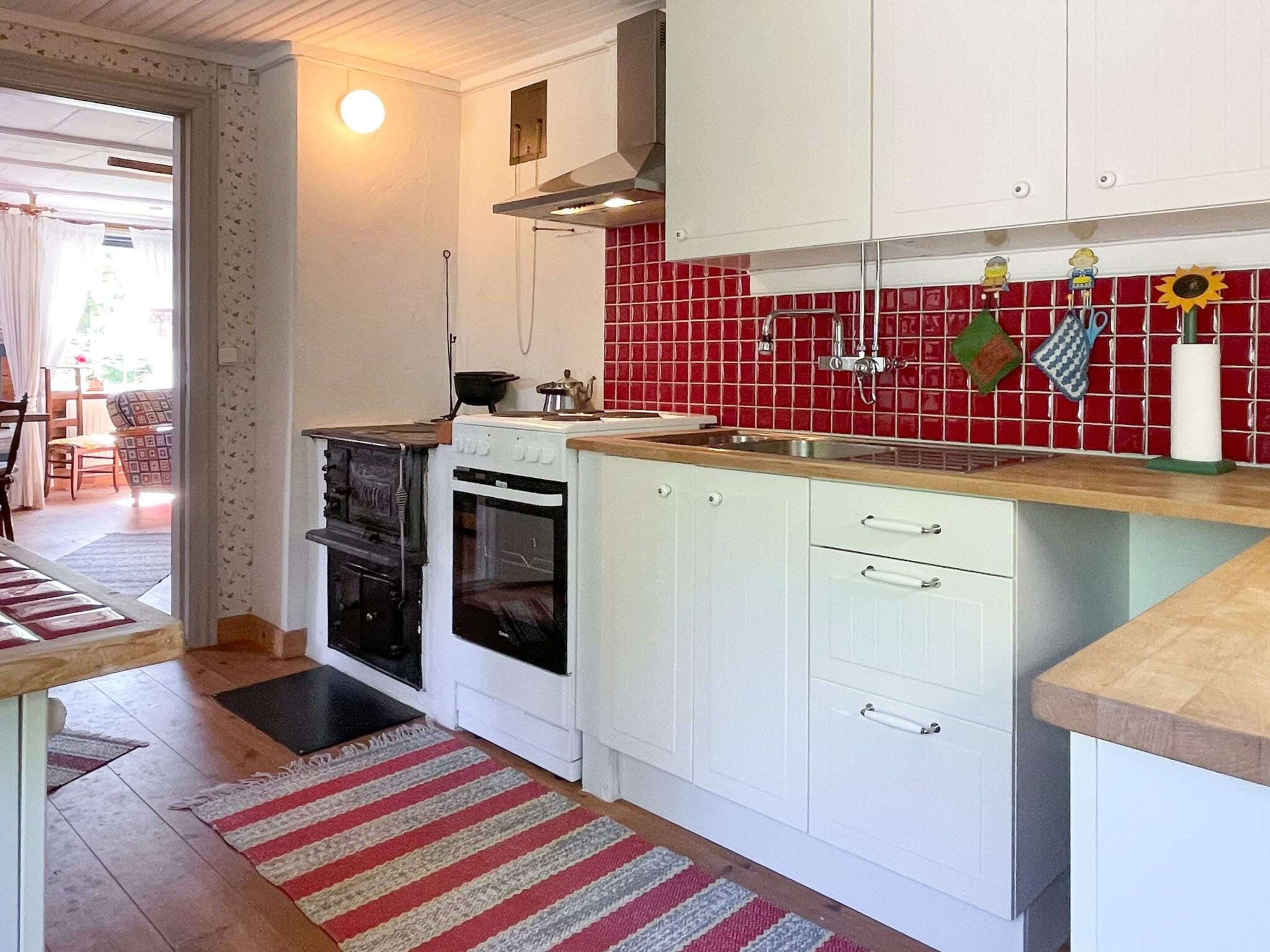 Een keuken met witte kasten, een rode tegelachtergrond, een kookplaat, een oven en een spoelbak.