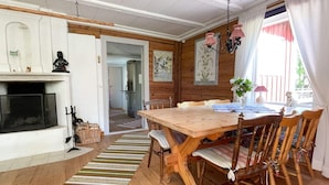 Une table à manger en bois, entourée de chaises, une cheminée et, au fond, une cuisine.