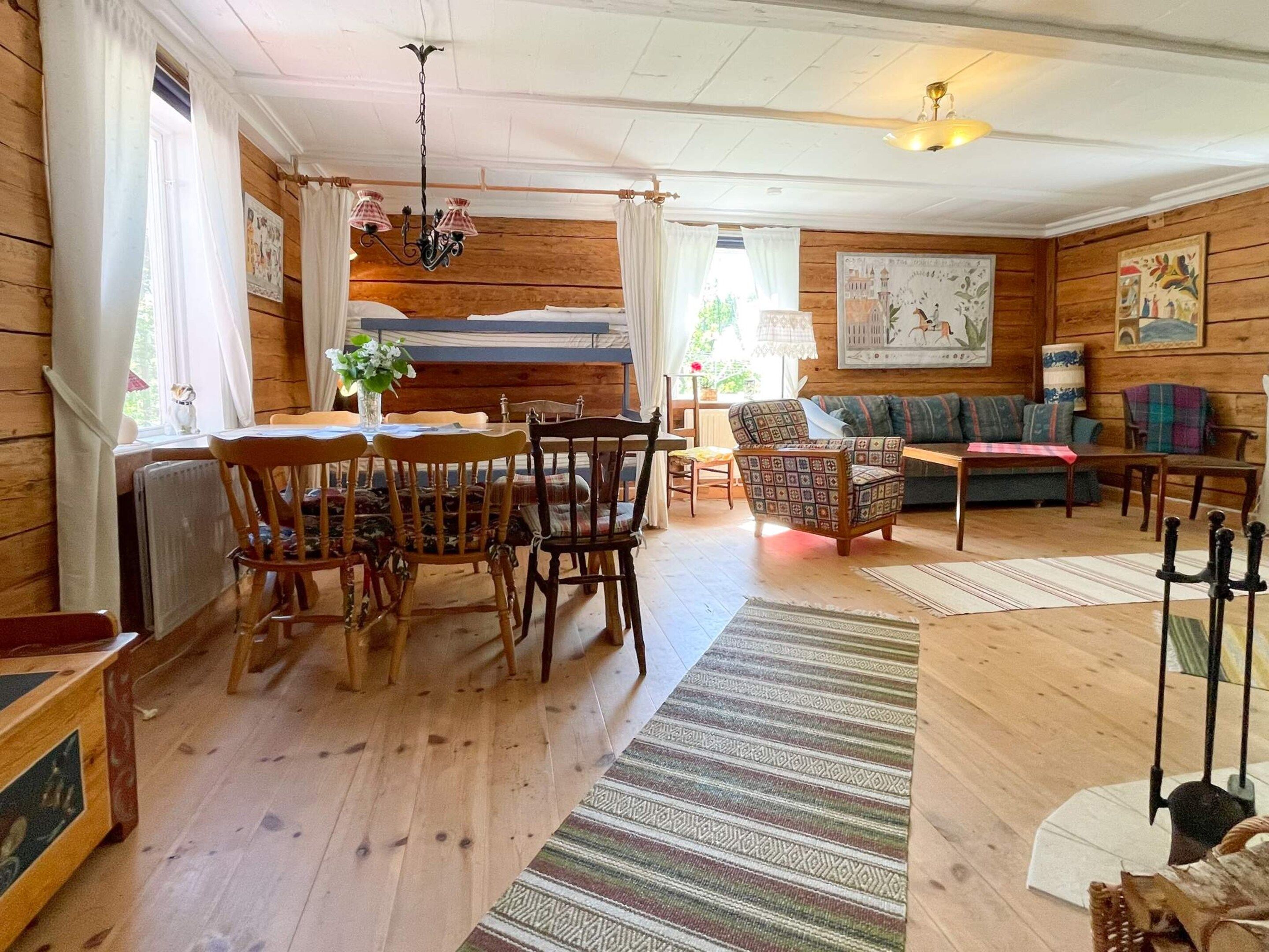 A wooden interior with a dining table, chairs, a sofa, and a patterned rug.