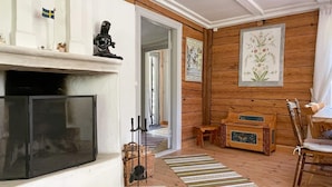 Un salon avec une cheminée, des murs en bois, un coin repas avec une table et des chaises, et un couloir avec une porte.