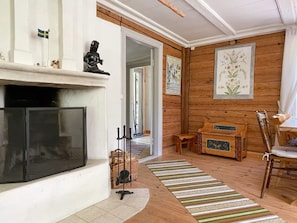 A living room with a fireplace, wooden walls, a dining area with a table and chairs, and a hallway with a door. - 5 Person Holiday Home in Ruda (Ruda)