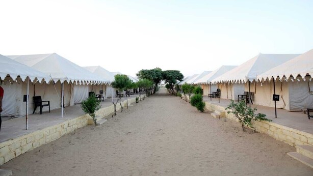 A row of white tents with a sandy path between them, each tent has a small table and chairs outside. - Mehta Desert Camp (Jaisalmer)
