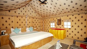 A room with a bed, a table with water bottles, a ceiling fan, and patterned walls. - Mehta Desert Camp (Jaisalmer)