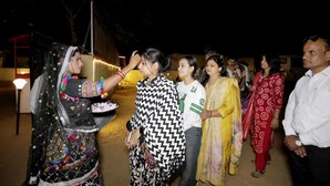 A group of people outdoors at night, some in traditional attire, gathered around a table with food. - Mehta Desert Camp (Jaisalmer)