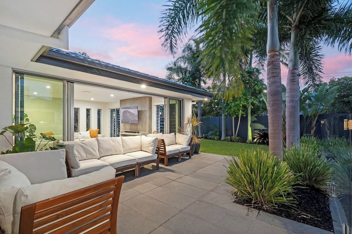 Een modern huis met terras, tuinmeubilair en tropische planten.