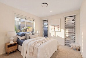 A bedroom with a bed, bedside tables, a window, and a door with blinds. - The perfect family home 400mtrs from Burleigh Beach & 300mtrs from James Street. (Burleigh Waters)