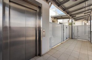 Puerta de ascensor metálica, entrada con reja y zona exterior cubierta con suelo de baldosas.