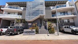 A modern building with a unique architectural design, featuring a central glass facade and multiple balconies. - Stylish Coastal Penthouse with Port Views (North Fremantle)