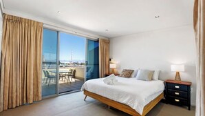 A hotel room with a bed, bedside tables, a view through a glass door to an outdoor area, and a balcony. - Stylish Coastal Penthouse with Port Views (North Fremantle)