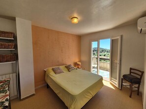 A bedroom with a bed, a chair, a shelf with baskets, a radiator, and a view through a sliding door. - Nice house, A/C, WIFI, garden, close to the beach (ST MANDRIER SUR MER)