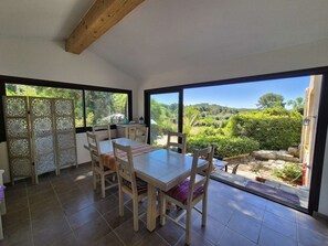 A dining area with a table and chairs, large windows with a view of greenery, and a wooden ceiling. - Nice house, A/C, WIFI, garden, close to the beach (ST MANDRIER SUR MER)