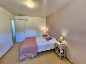 A bedroom with a bed, bedside tables, a wall-mounted air conditioner, and a door. - Nice house, A/C, WIFI, garden, close to the beach (ST MANDRIER SUR MER)
