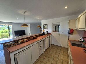 A compact kitchen with a central island, a built-in TV, pendant lighting, and a view of greenery outside. - Nice house, A/C, WIFI, garden, close to the beach (ST MANDRIER SUR MER)