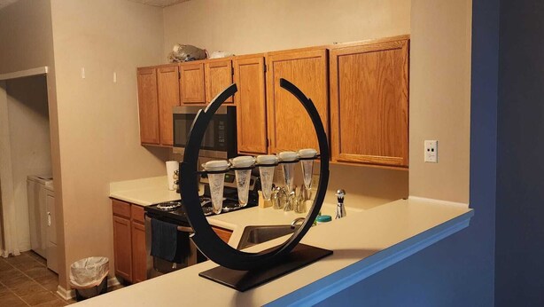 A kitchen with wooden cabinets, a microwave, a stove, and a unique black circular object on the counter. - 2 Master bedrooms condo with Two walk in Closets and half bath main floor (Indianapolis)