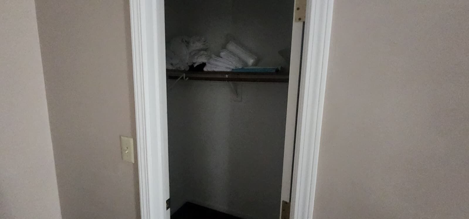 A narrow hallway with a door leading to a closet containing folded clothes on a shelf.