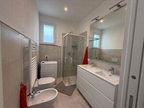 A modern bathroom with a toilet, bidet, sink, and a glass-enclosed shower. - Appartamento Montecristo - Montecristo (Capoliveri)