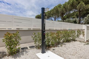 Eine Solaranlage mit einem Steuerungskasten, umgeben von Kies und kleinen Sträuchern, vor dem Hintergrund eines weißen Zauns und Bäumen.
