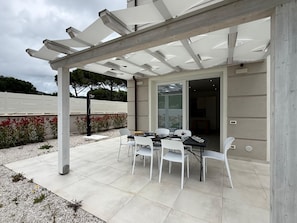 An outdoor patio with a pergola, a table with chairs, and a view of the interior. - Appartamento Montecristo - Montecristo (Capoliveri)