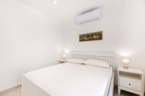 Ein Schlafzimmer mit einem Bett, Nachttischen, einer Klimaanlage und einem Wandbild.