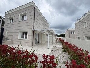 A modern residential building with a covered patio area, a gated entrance, and a gravel pathway. - Appartamento Montecristo - Montecristo (Capoliveri)