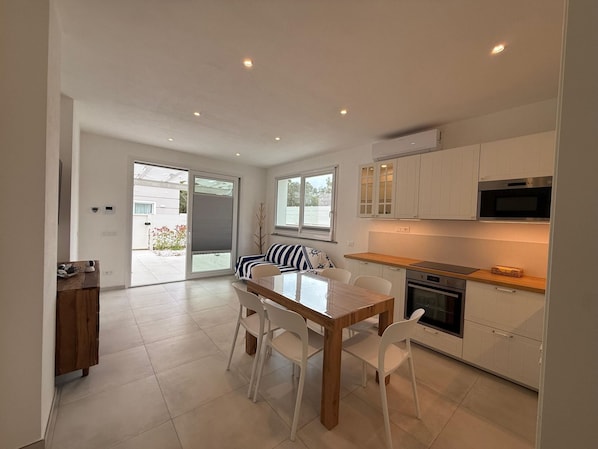 A modern kitchen with white cabinets, a wooden countertop, and a dining area with a white table and chairs. - Appartamento Montecristo - Montecristo (Capoliveri)