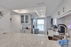 A modern kitchen with a marble countertop, built-in appliances, and a view to the dining area. - Wake to the Waves | Stunning Sunsets | Quiet South End, Gulf-Front Retreat | Heated Pool & Sun Deck (Fort Myers Beach)